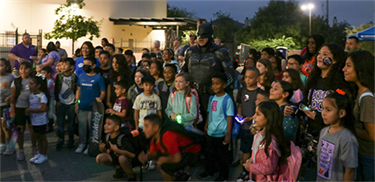 Batman standing in the middle of a group of children and adults.