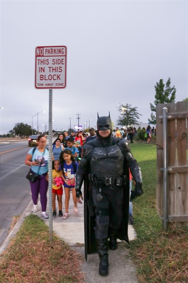 Batman leading a group of children and adults on their walk to school.