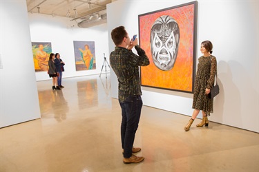 A man takes a photo of a woman standing next to a large painting.