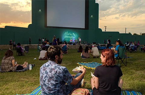 Couple watching outdoor movie with crowd at sunset.