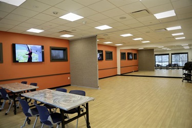 Activity room with orange walls, half-wall, mirror, tv, tables and chairs