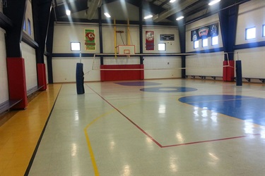 A gymnasium with a volleyball net and a basketball hoop, providing sports facilities for various activities.