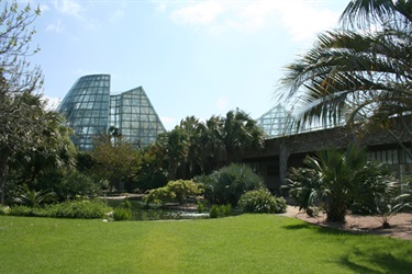 A serene landscape with lush green grass, tall trees, and Conservatory building in the background.