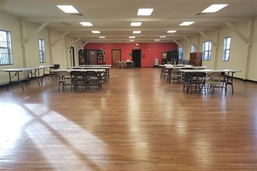 Room with red and white walls with 7 tables and 5 to 6 chairs at each table