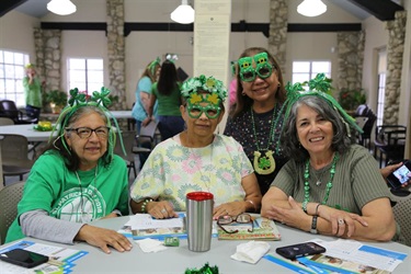 Four women wearing green and shamrock masks, celebrating St. Patrick's Day.