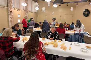 Large group of people gathered around tables making tamales.