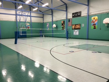 Indoor gymnasium with a volleyball net and basketball hoops.