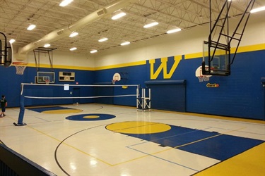 A volleyball court in a gym with a net and a basketball hoop.