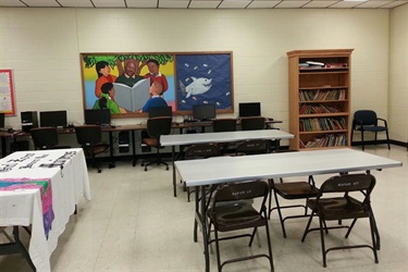 A classroom with tables and chairs arranged in front of a large painting depicting an inspiring scene.
